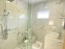 Modern bathroom with marble walls, glass shower, and white fixtures