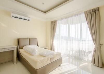 Bright bedroom with an air conditioner, bed, desk, chair, and large windows with curtains
