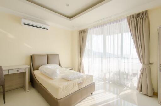 Bright bedroom with an air conditioner, bed, desk, chair, and large windows with curtains
