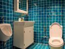 Modern bathroom with blue tiled walls and floor, featuring a toilet, urinal, and vanity with mirror cabinet