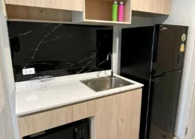 Compact kitchen with wooden cabinets, black refrigerator, sink, and microwave