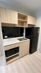 Compact kitchen with wooden cabinets, black refrigerator, sink, and microwave