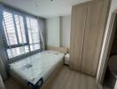 A modern bedroom with a large window, wooden wardrobe, and a mattress on a wooden bed frame.