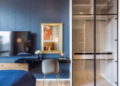 Modern bedroom with blue accent wall, wall-mounted TV, study table with chair, and walk-in closet