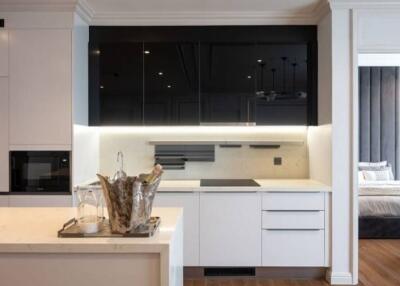 Modern kitchen with white cabinets, black upper cabinets, and integrated appliances adjacent to open bedroom