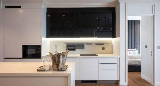 Modern kitchen with white cabinets, black upper cabinets, and integrated appliances adjacent to open bedroom