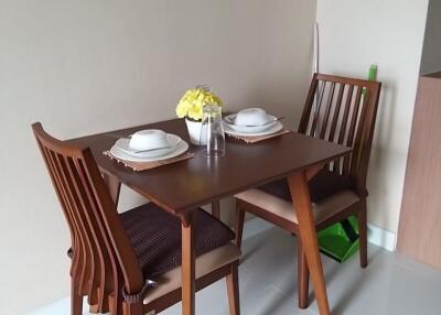 Small dining area with wooden table and chairs, set with dishware and a vase with yellow flowers