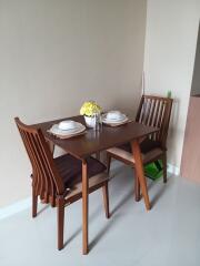 Small dining area with wooden table and chairs, set with dishware and a vase with yellow flowers