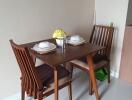 Small dining area with wooden table and chairs, set with dishware and a vase with yellow flowers