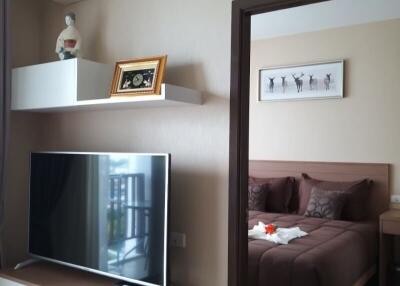 Living area featuring a TV and wall shelves, with a view into a bedroom