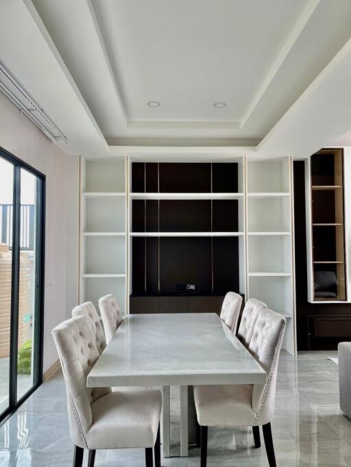 Modern dining room with a white table and cushioned chairs, featuring built-in shelves.