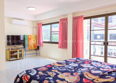 Spacious and brightly lit bedroom with colorful décor, large windows, and a TV.