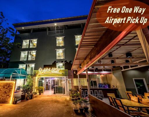 Night view of a modern building with outdoor lounge and sign offering free one-way airport pick up