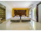 Modern bedroom with two beds and a yellow accent wall, adjacent bathroom, and a sliding door leading to a balcony.