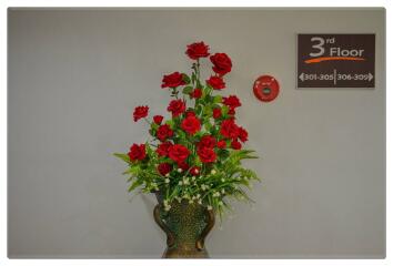 Decorative vase with red flowers near floor indicator sign