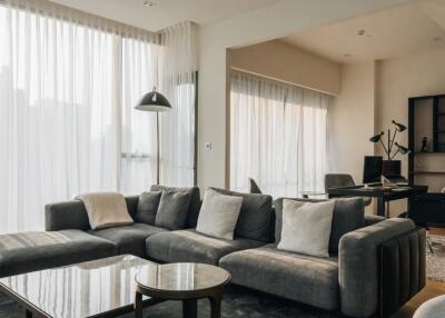 Modern living room with large windows, gray sectional sofa, and a home office area