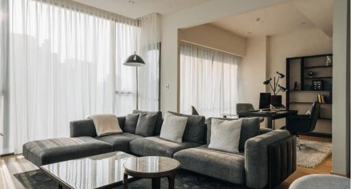 Modern living room with large windows, gray sectional sofa, and a home office area