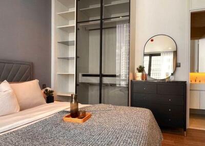 Modern bedroom with a bed, an open wardrobe, a chest of drawers with a mirror, and an ensuite bathroom