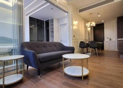 Modern living room with dark grey sofa, coffee tables, and adjacent dining area with stylish chandelier.