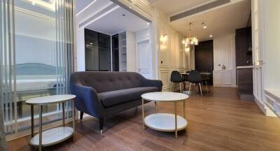 Modern living room with dark grey sofa, coffee tables, and adjacent dining area with stylish chandelier.