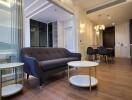 Modern living room with dark grey sofa, coffee tables, and adjacent dining area with stylish chandelier.