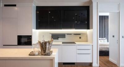 Modern kitchen with white cabinetry, black accent panels, and an adjacent bedroom visible through open door