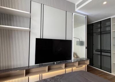 Modern bedroom with mounted TV, shelves, and mirrored wardrobe