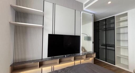 Modern bedroom with mounted TV, shelves, and mirrored wardrobe