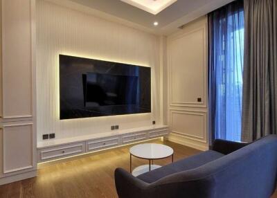 Modern living room with built-in shelves, a flat-screen TV, and large windows with curtains