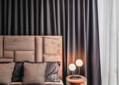 A modern bedroom with a tufted headboard, black and white pillows, a nightstand, two round lamps, and dark curtains