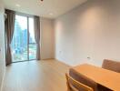 Bright living area with wood flooring, showing a table and chairs near a large window with city views