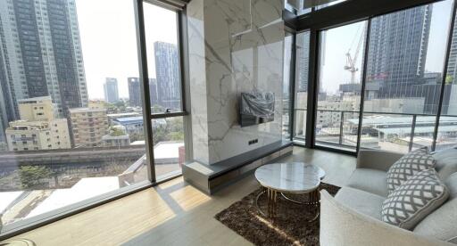 Modern living room with large windows, city view, marble coffee table, and mounted TV