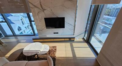 Modern living room with large windows, marble wall feature, and mounted TV