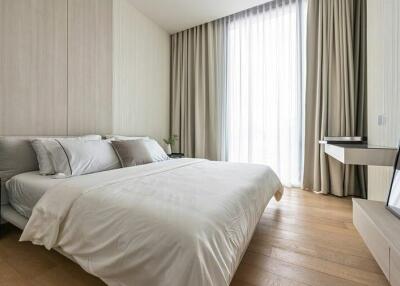 Modern bedroom with a large bed, wooden floor, and a tall window with floor-to-ceiling curtains