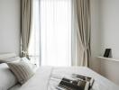 Modern bedroom with a large window, white curtains, and neatly arranged bedding