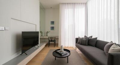 Modern living room with gray sofa, TV, and full-length windows with sheer curtains