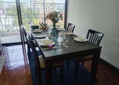 A modern dining room with a table set for four, featuring a view of a balcony and cityscape.