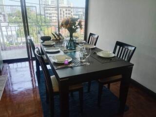 A modern dining room with a table set for four, featuring a view of a balcony and cityscape.