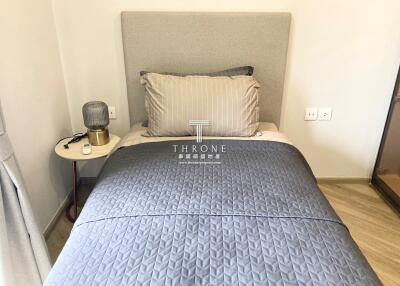 Compact bedroom with a neatly made bed featuring grey bedding, and a nightstand with a lamp.