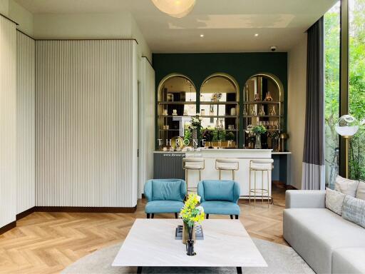 Modern living room with a contemporary design featuring blue armchairs, a white coffee table, a cushioned sofa, and a bar area with stools and decorative shelves.