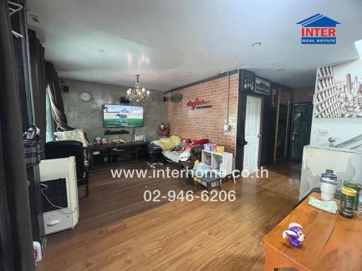 Living room with wooden flooring, brick accent wall, TV, couches, and chandelier