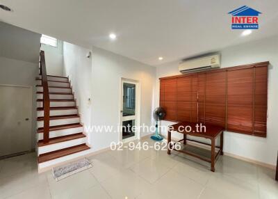 Living room with stairs, air conditioner, wooden blinds, and a desk