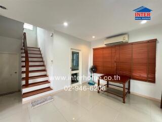 Living room with stairs, air conditioner, wooden blinds, and a desk