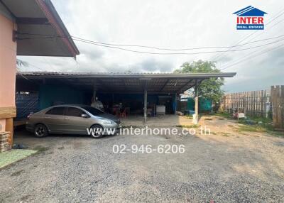 Carport area with vehicle parked under metal roof, gravel driveway, partial view of house and fence