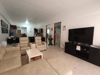 Modern living room with beige sofas, a large TV, and open access to kitchen