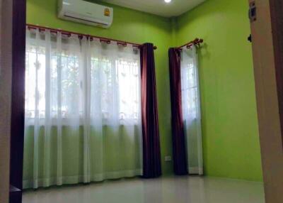 A well-lit bedroom with green walls, large windows, and an air conditioner