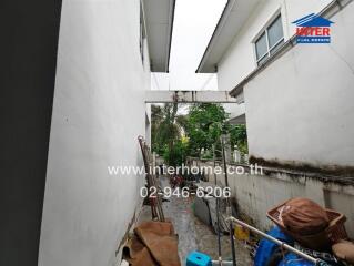 Outdoor area between two buildings with miscellaneous items and some greenery