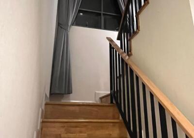 Wooden staircase with black railing and large window with gray curtains