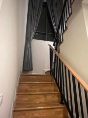 Wooden staircase with black railing and large window with gray curtains