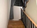 Wooden staircase with black railing and large window with gray curtains